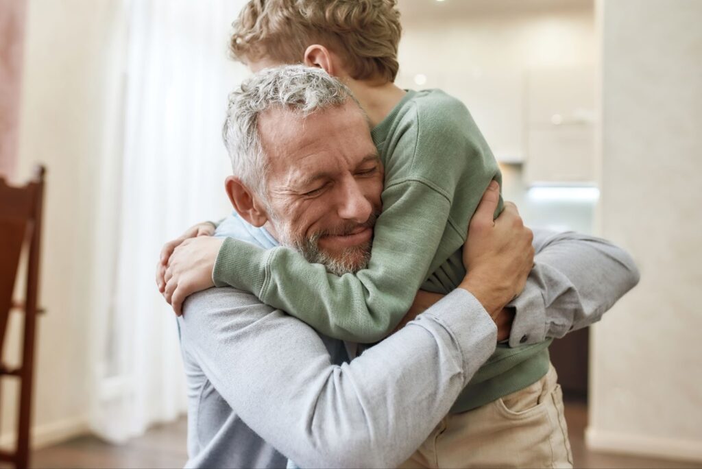 A grandfather with dementia smiles and hugs his grandchild