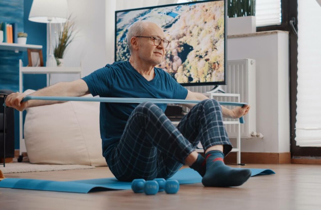 Senior man exercising with a resistance band on a yoga mat in a small living room.