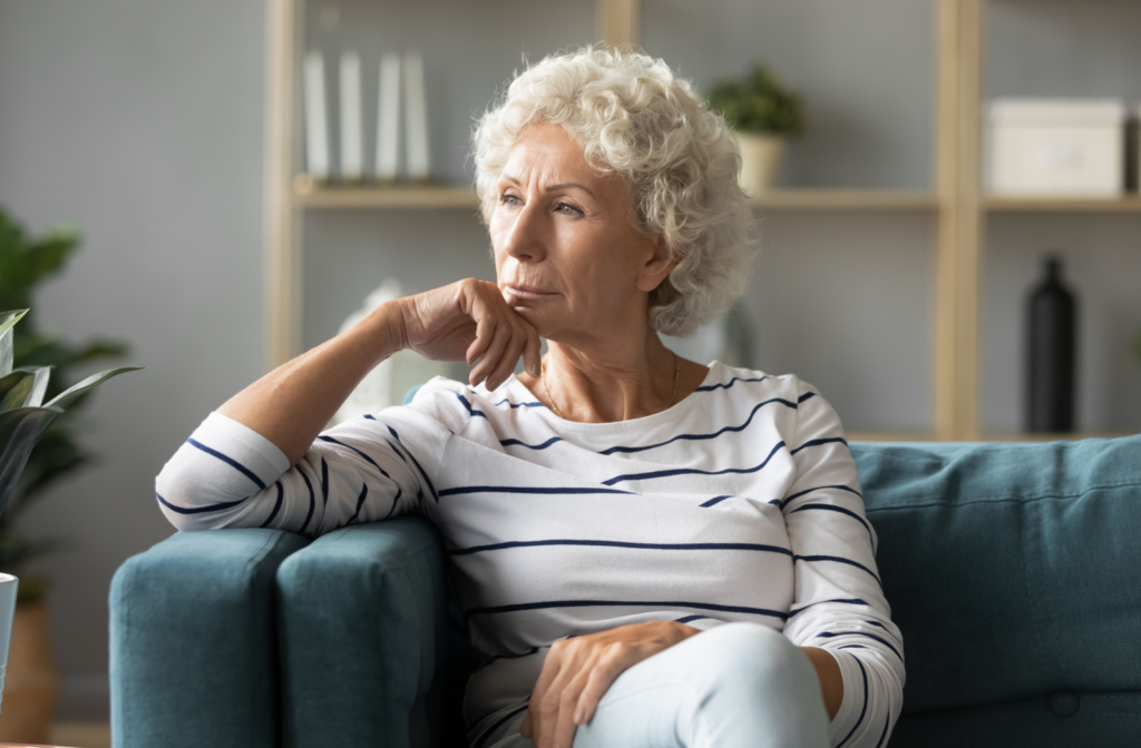 A senior sits on a comfy couch, gazing contemplatively out of the window.